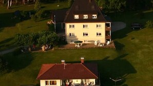 A two-story house with a balcony, surrounded by a well-maintained lawn and trees. - Apartment "Lindau" with Shared Terrace, Garden, and Wi-Fi (Uhldingen-Mühlhofen)