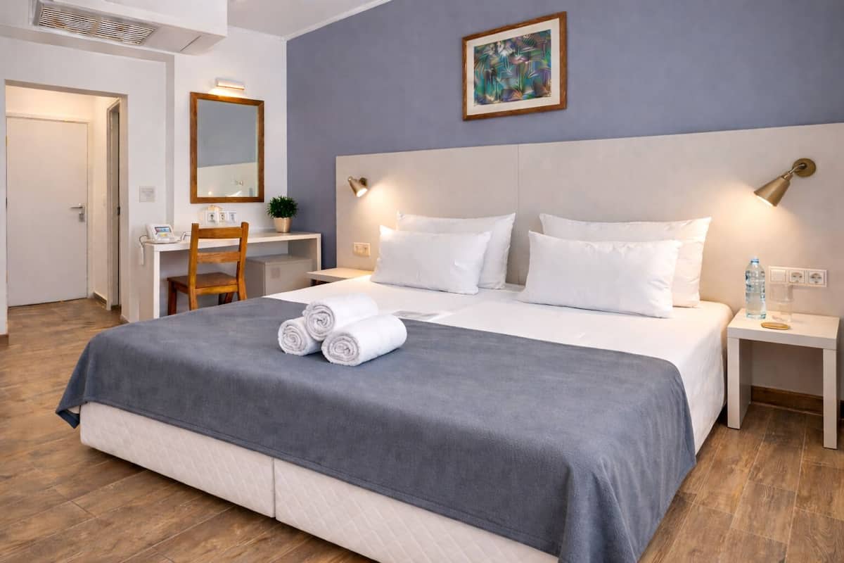Une chambre d’hôtel comprenant un lit, des tables de chevet, un bureau, une chaise, un miroir et un tableau accroché au mur.