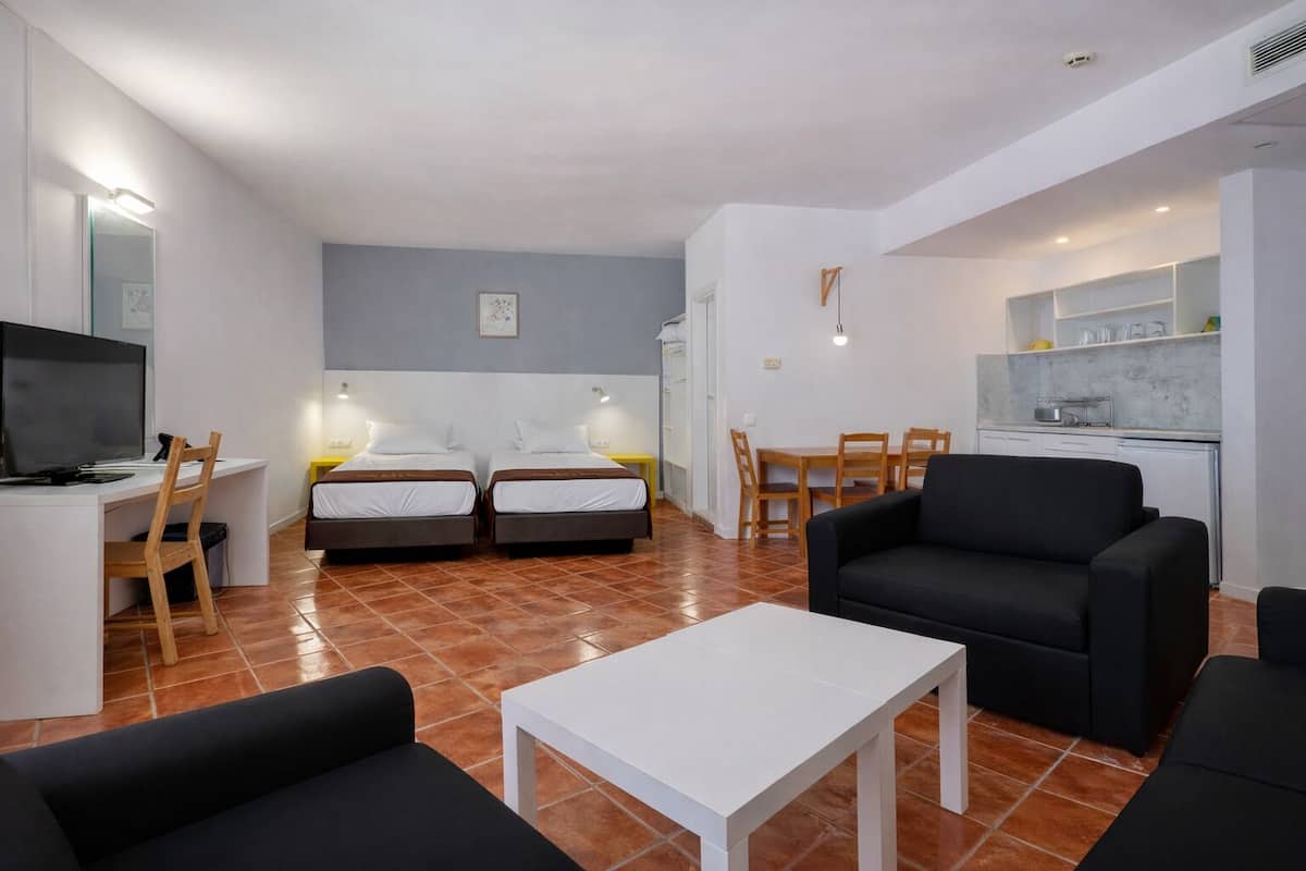 Une pièce moderne et bien éclairée, comprenant un lit, un bureau, une télévision, un canapé noir et un coin repas.