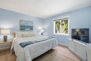 Ein Schlafzimmer mit einem Bett, zwei Nachttischlampen, einem Fernseher, einem Fenster mit Blick und einem Bild an der Wand.