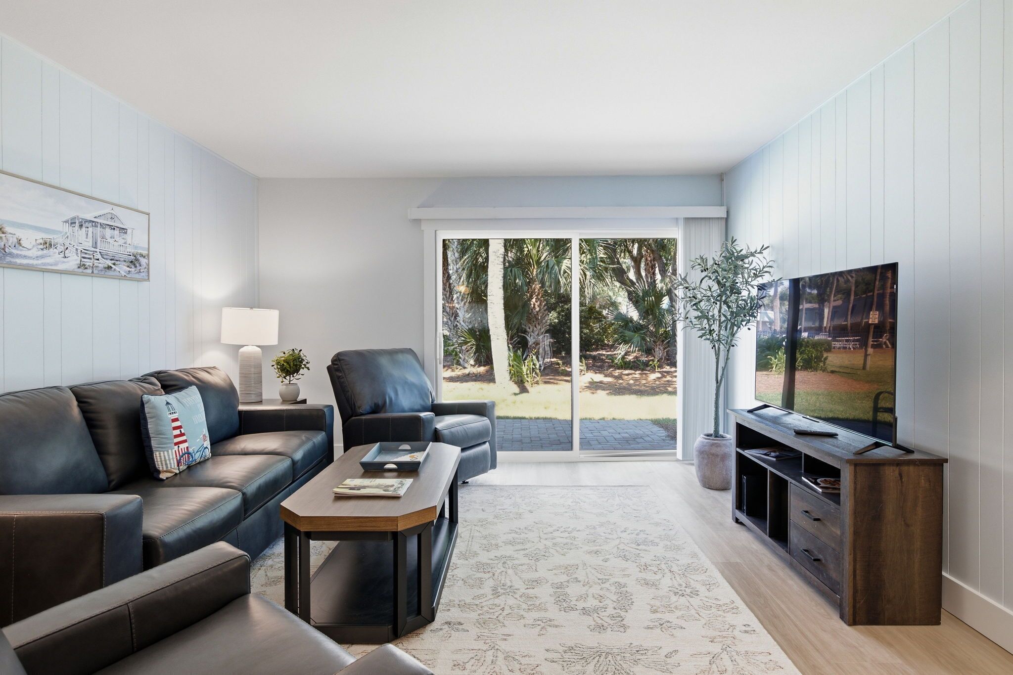 A modern living room with a sofa, coffee table, TV, and a sliding glass door leading to a garden.