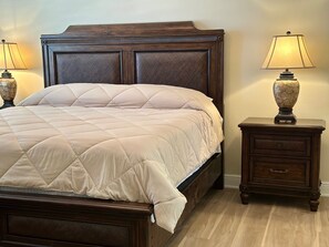 Una cama con cabecera acolchada, dos mesitas de noche con lámparas y suelo de madera.