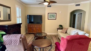Een woonkamer met een bank, fauteuil, salontafel, televisie en open haard.