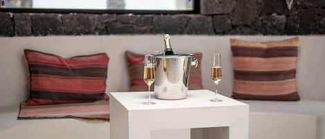 A white table with a champagne bucket and two glasses of champagne on a white sofa with striped pillows.