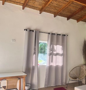 A room with a window, a chair, a table, and a ceiling with wooden beams.