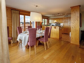 A dining area with a table set for four, wooden flooring, and a kitchen with wooden cabinets. - Pré Vert by Interhome (Villars)
