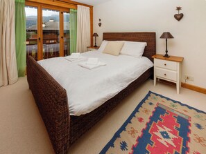 A bedroom with a large bed, a nightstand with a lamp, a dresser, and a view through a sliding glass door. - Pré Vert by Interhome (Villars)