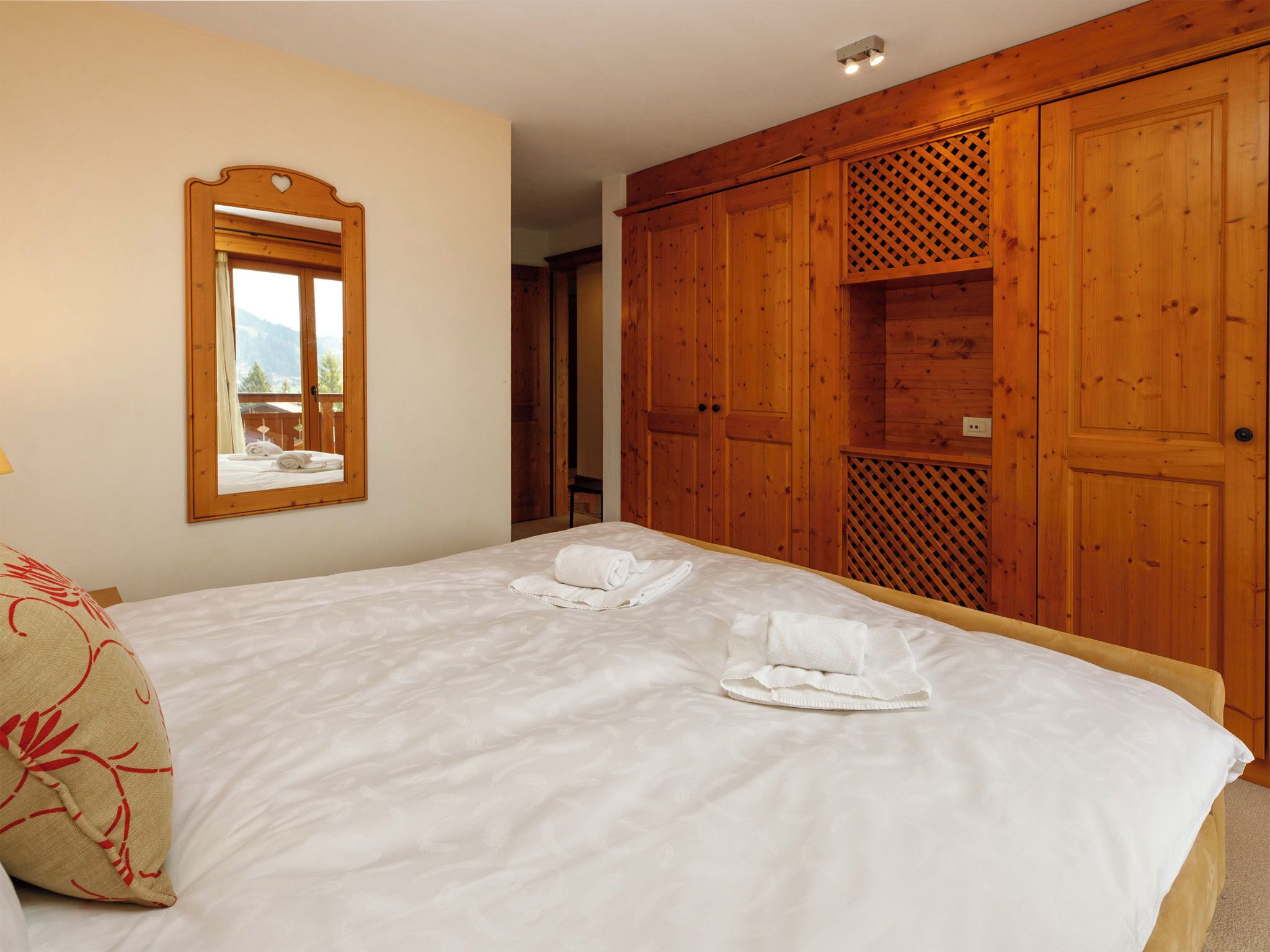 Une chambre à coucher avec un lit, un miroir, une armoire en bois et une fenêtre donnant sur un beau paysage.