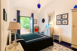 Ein Schlafzimmer mit einem Bett, einer Lampe, einem Sessel, einem kleinen Tisch, einem Schrank und einer Tür, die auf einen Balkon führt.