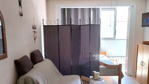 Un dormitori amb un llit, una taula petita, un armari i una finestra amb cortines.