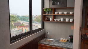 A kitchen with a window, wooden cabinets, a sink, and shelves with cups and a plant. - Hoa Gió Boutique Stay (Hue)