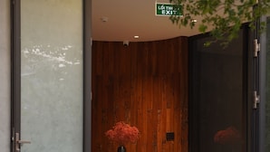 A modern interior with a wooden wall, a glass door, a sofa, a table, and a vase with red flowers. - Hoa Gió Boutique Stay (Hue)