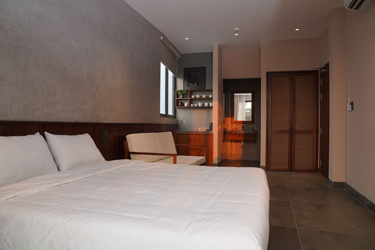 Una camera d'albergo con un letto grande, una poltrona, una scrivania e un armadio.