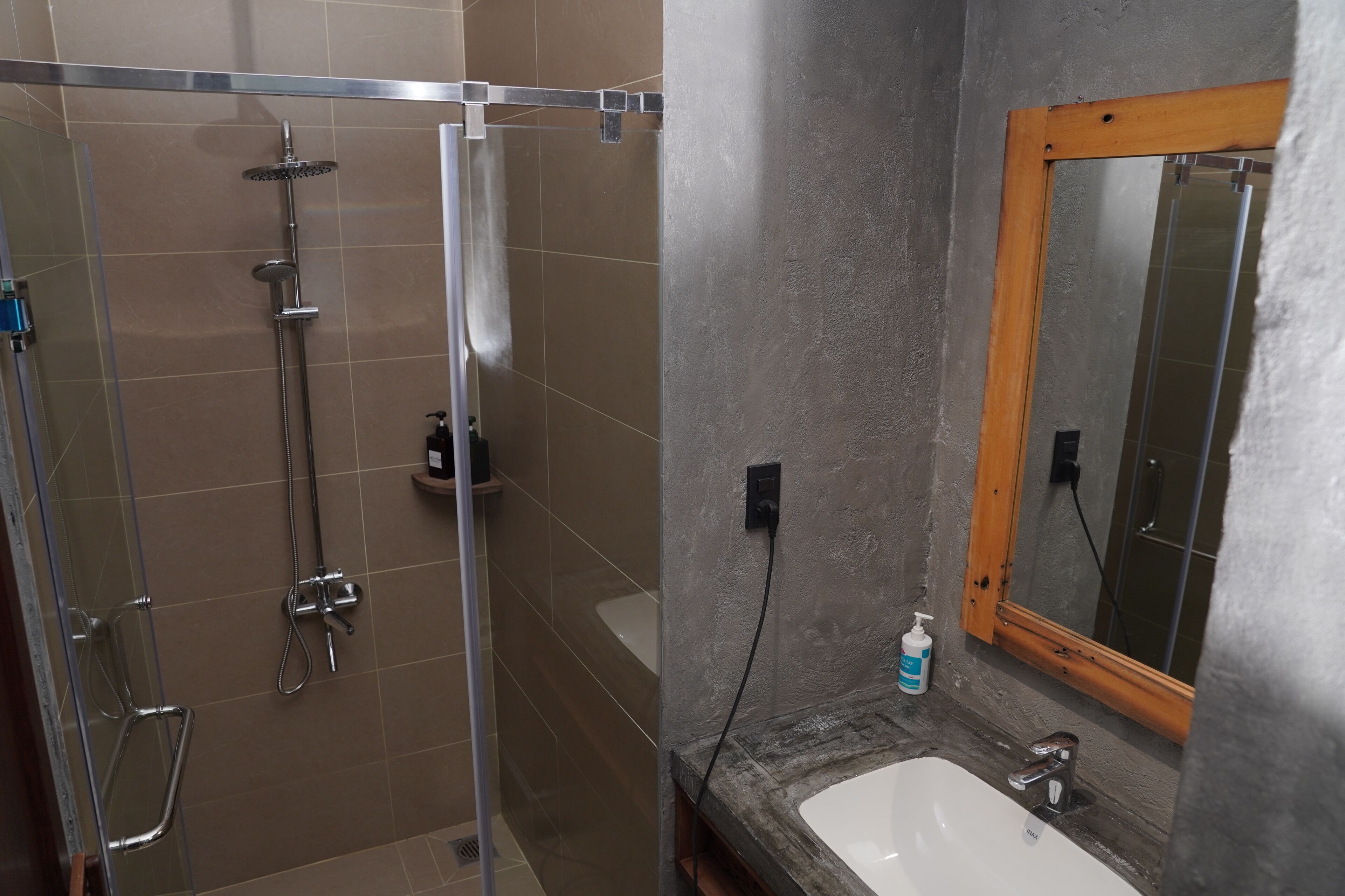 A bathroom with a glass-enclosed shower, a white sink, and a mirror with a wooden frame.