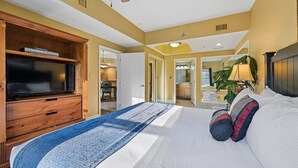 A bedroom with a large bed, a wooden entertainment unit, and a view of the kitchen and living area. - Baskins Creek 212 🐻 Sleeps 6 | Pool Views, Hot Tub & Stone Fireplace 🔥 (Gatlinburg)