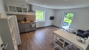 A modern kitchen with a built-in oven, a dining area with a table and chairs, and a large window providing a view of the outdoors. - Apartment 'Fewo Am Adlerweiher' with Shared Terrace, Shared Garden and Wi-Fi (Feldberg (Schwarzwald))
