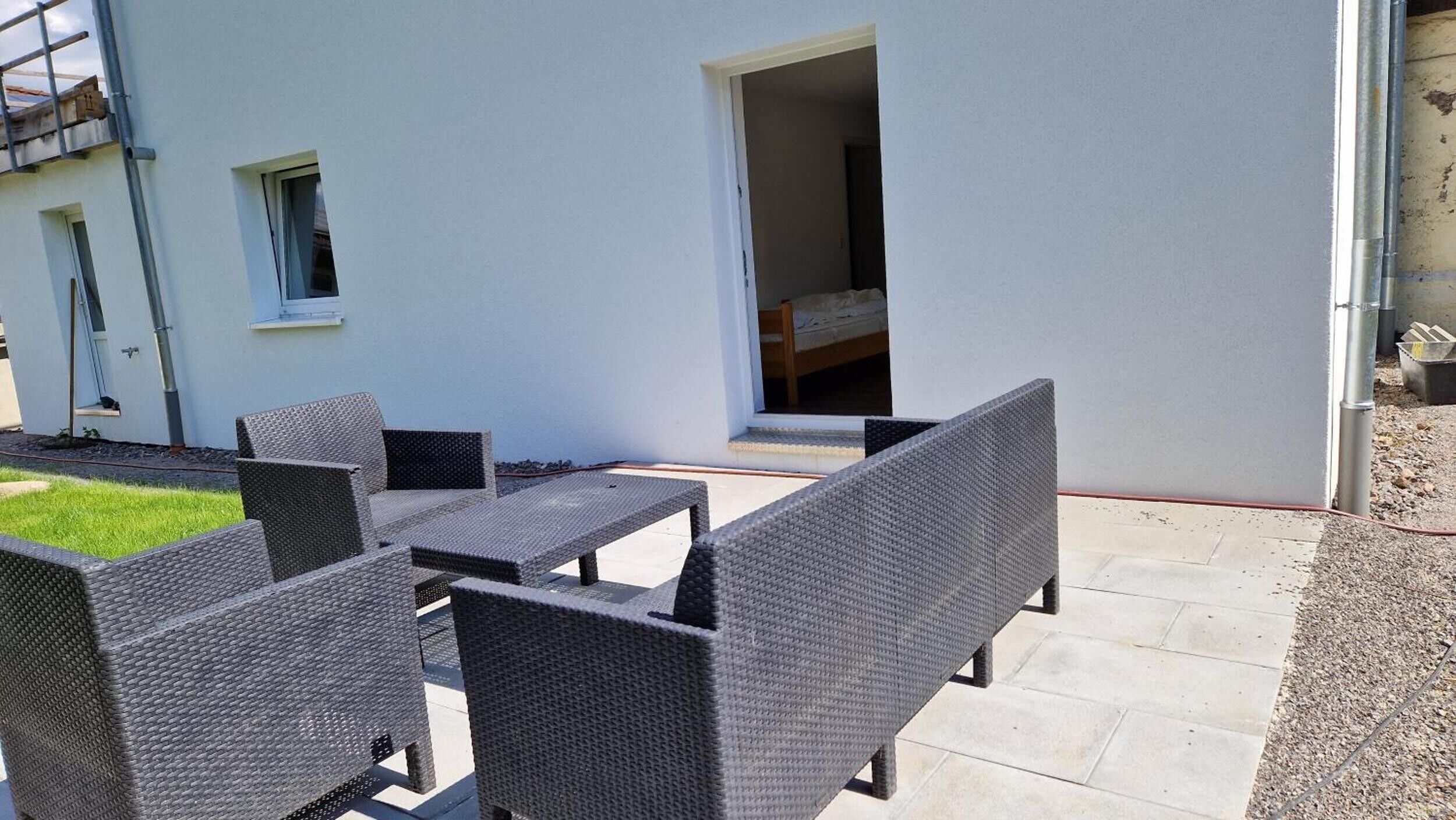 A patio with wicker furniture, a white building, and a doorway leading to a room.