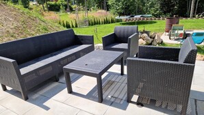 An outdoor patio with wicker furniture, including a sofa and two chairs, a small table, and a trampoline in the background. - Apartment 'Fewo Am Adlerweiher' with Shared Terrace, Shared Garden and Wi-Fi (Feldberg (Schwarzwald))