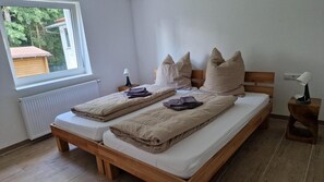 A double bed with a wooden frame, two bedside tables with lamps, a window with blinds, and a radiator.