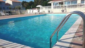Una piscina con escalera metálica, sillas de descanso y valla blanca.
