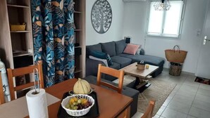 Una sala de estar con un sofá, una mesa de comedor con una cesta de fruta y una obra de arte colgada en la pared.