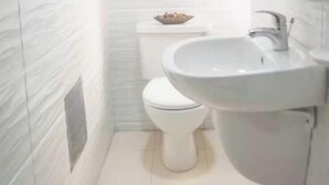 Une petite salle de bain blanche, avec des toilettes, un lavabo et un miroir.