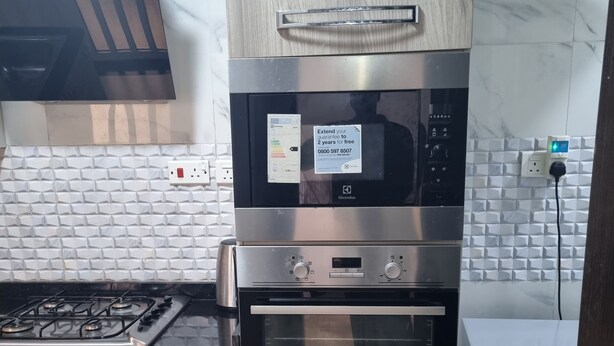 Une cuisine équipée d’un four à micro-ondes, d’un four et d’une cuisinière encastrés, de meubles de rangement en bois et d’un réfrigérateur Hisense.