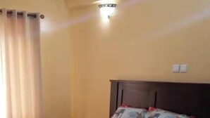 Un lit simple avec une tête de lit, une table de chevet, un rideau et un luminaire fixé au mur.