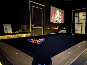 A billiards table with balls, a fireplace, and a projection screen displaying a fire.