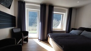 A bedroom with a bed, a chair, a TV, and a window with curtains. - Comfort Breakfast Room with Balcony and Moselle View for 2 in Ediger-Eller (20 m²) (Ediger-Eller)