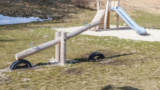 Un terrain de jeux avec un toboggan et une balançoire, situé dans un cadre vallonné.