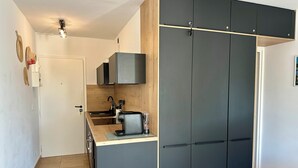 A compact kitchen with a countertop, a sink, and a stove. There is a wooden cabinet with a black door and a white door leading to another room. - L'Eden in Downtown Saint-Tropez with a Pool (Saint-Tropez)