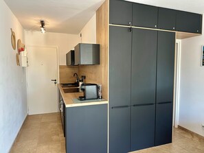 A compact kitchen with a countertop, a sink, and a stove. There is a wooden cabinet with a black door and a white door leading to another room. - L'Eden in Downtown Saint-Tropez with a Pool (Saint-Tropez)