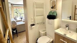 A bathroom with a toilet, sink, and a shower area. There is a towel rack above the sink and a framed picture on the wall. - L'Eden in Downtown Saint-Tropez with a Pool (Saint-Tropez)