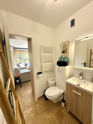 A bathroom with a toilet, sink, and a shower area. There is a towel rack above the sink and a framed picture on the wall. - L'Eden in Downtown Saint-Tropez with a Pool (Saint-Tropez)
