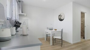 Et moderne køkken med hvide hårde hvidevarer, et spiseområde med bord og stole samt et billede hængt på væggen.