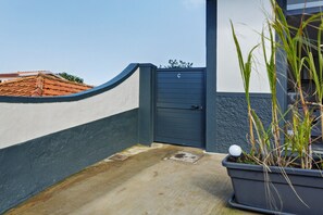 Een hekpoort met een blauwe deur, een betonnen pad en een plantenpot met hoog gras.