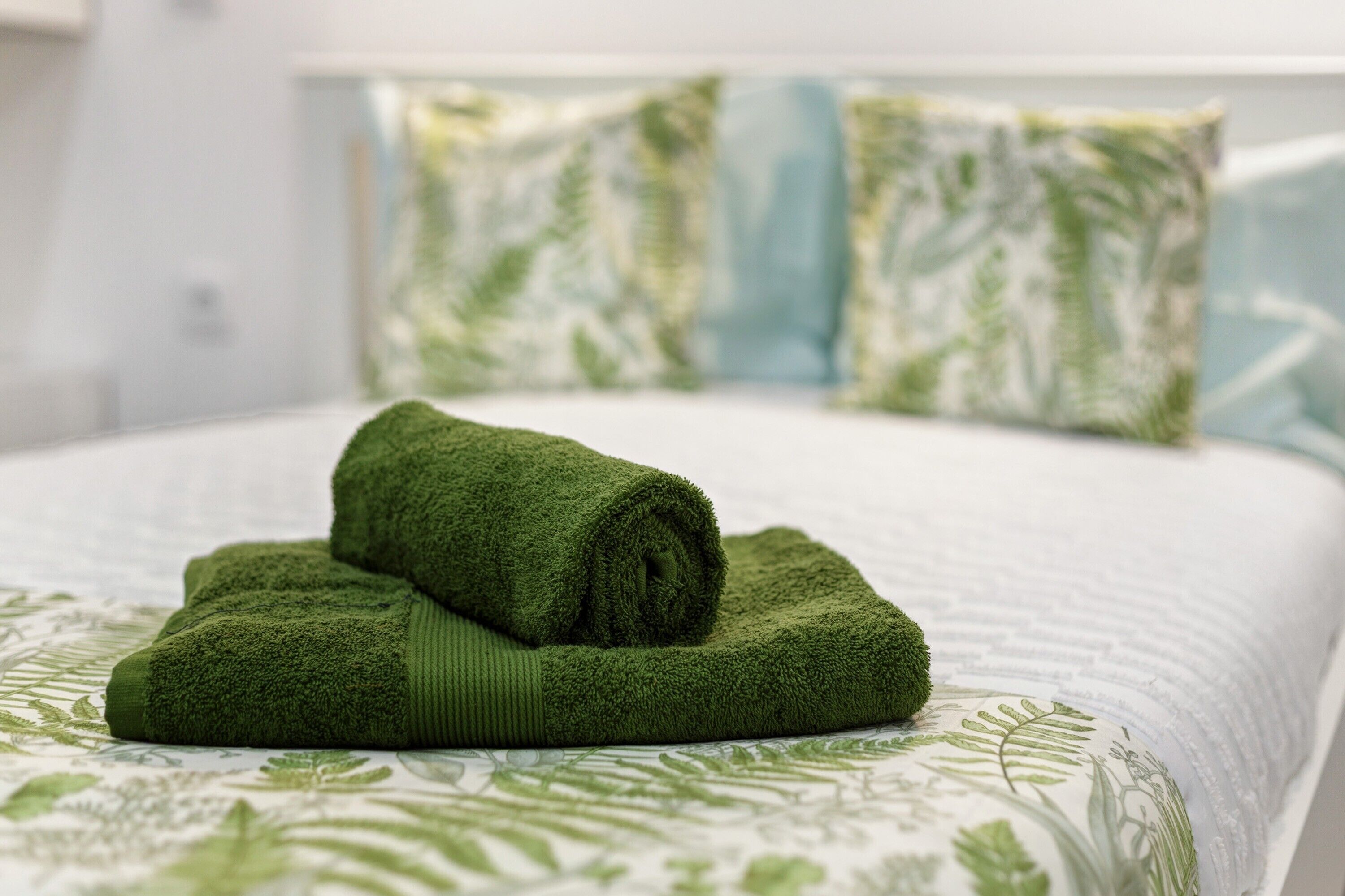 Un lit bien fait, avec une serviette verte, une couvre-lit à motifs et des coussins assortis.