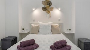 Ein ordentlich bezogenes Bett mit zwei zusammengerollten Handtüchern, Wandbild mit einem Blatt und Nachttische mit kleinen Pflanzen.