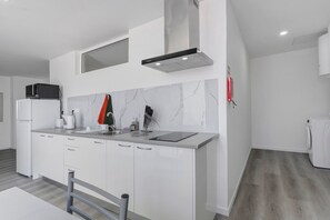 Una cocina moderna con gabinetes blancos, una campana extractora de acero inoxidable, un microondas y un lavamanos.