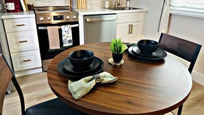 A modern kitchen with white cabinets, a stainless steel range, and a wooden dining table set for two. - Designer Luxe Studio | King Suite + Work Space (Sacramento)