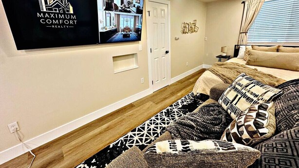 A living room with a flat-screen TV mounted on the wall, a sofa with patterned cushions, a wooden floor, and a door with a small window. - Designer Luxe Studio | King Suite + Work Space (Sacramento)