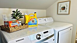 A Samsung washing machine with a basket of laundry detergent and a plant on top. - Designer Luxe Studio | King Suite + Work Space (Sacramento)