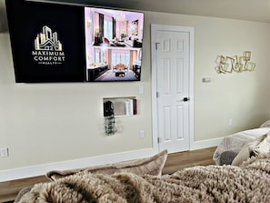 Ein modernes Wohnzimmer mit einem Flachbildfernseher, der ein Immobilienvideo zeigt, einer weißen Tür und einem Wandbild.