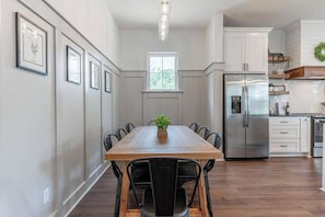 A dining area with a wooden table, black chairs, and a potted plant. A stainless steel refrigerator and white cabinets are visible in the background. - Haven House, Family Favorite (Waco)