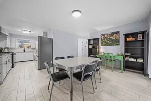 A modern kitchen with white cabinets, a dining table with chairs, and a green chair. - Work and Ride Downtown Edge 3BD Bentonville (Bentonville)