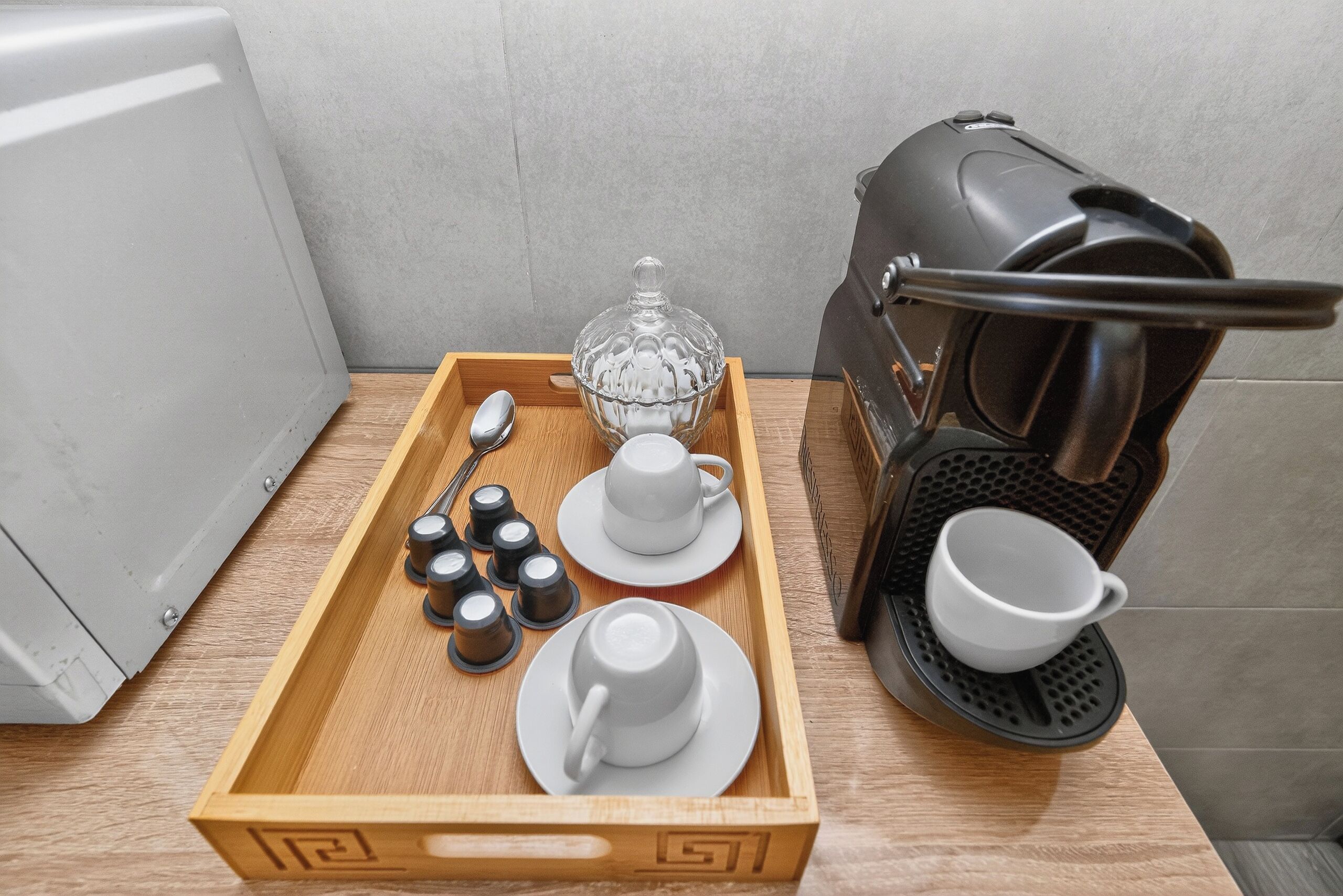 A tray with cups, a glass carafe, and a coffee maker on a wooden table.