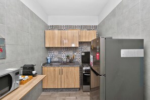 A compact kitchen with grey tiles, wooden cabinets, a stainless steel refrigerator, a microwave, and a coffee maker. - Central 2BR Marrakech · A/C · Workspace · Parking (Marrakesh)