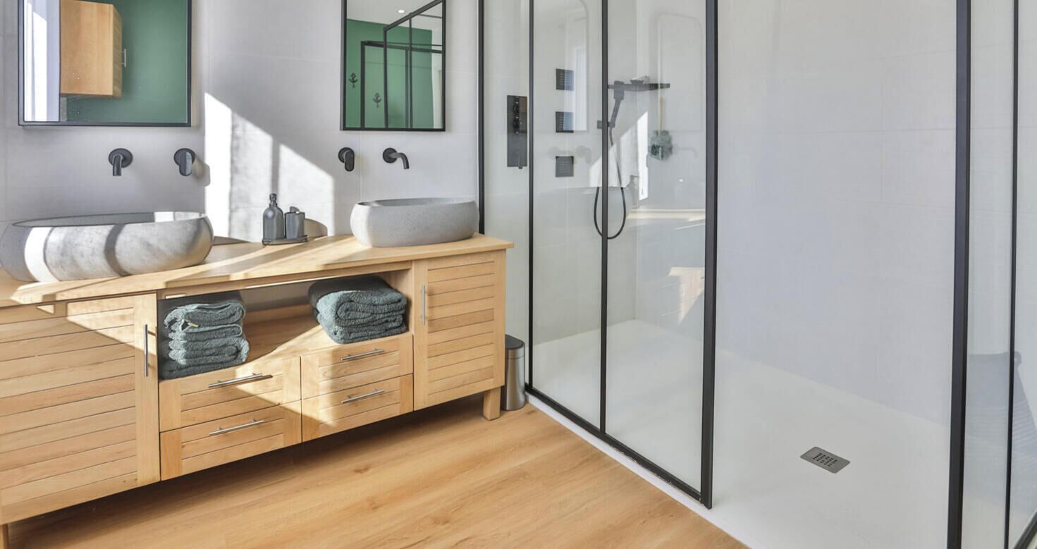 Un baño moderno con tocador de madera, un lavabo tipo recipiente, cabina de ducha de vidrio y un espejo con marco verde.