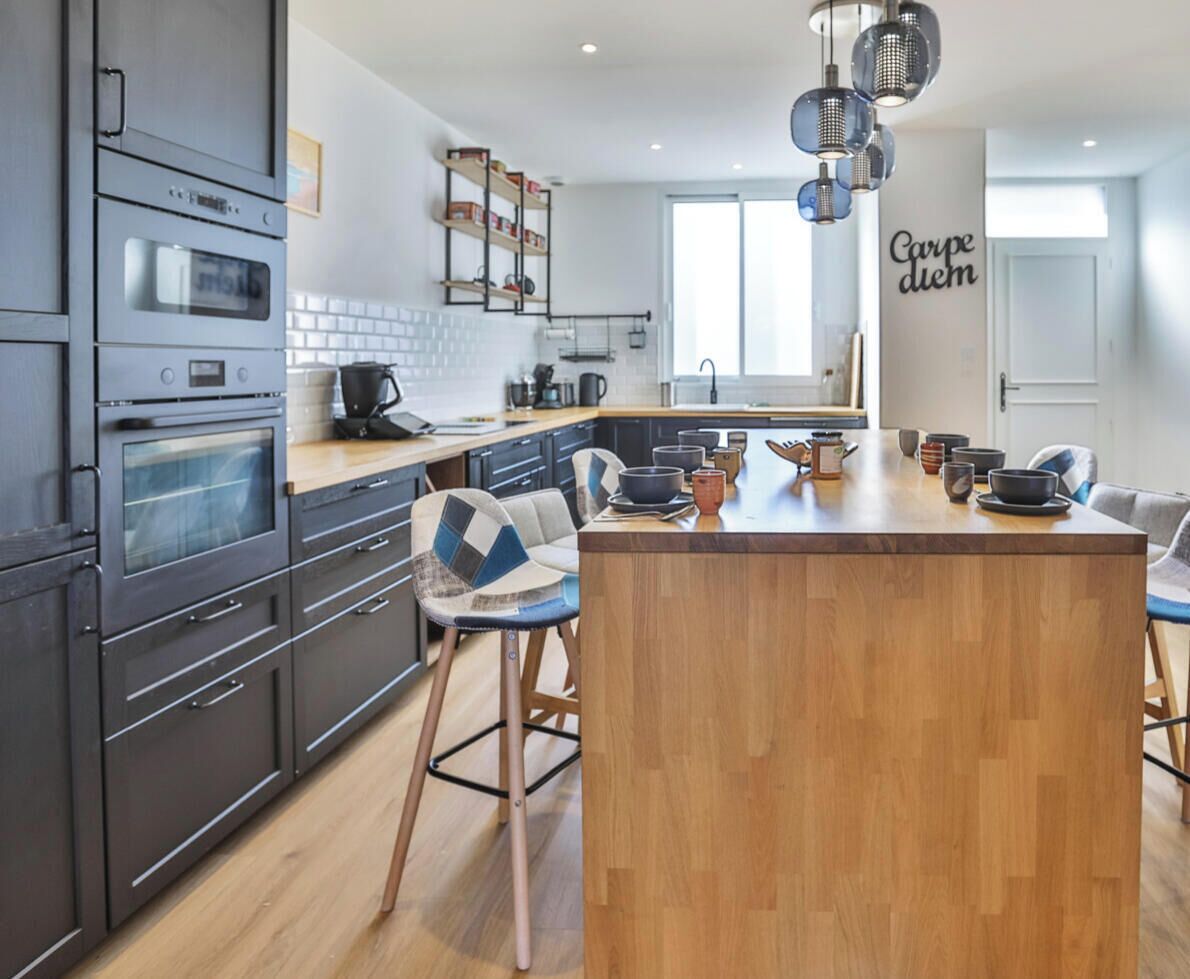 A modern kitchen with built-in appliances, a central island, bar stools, and a decorative wall sign.
